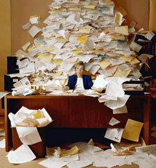 Overwhelmed office worker at desk covered with mountain of papers